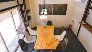 Une table en bois entourée de six chaises, un vase rempli de fleurs et un luminaire suspendu dans une pièce dotée d’une grande fenêtre et d’une œuvre d’art accrochée au mur.