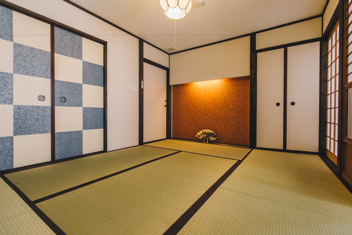 Una habitación japonesa tradicional con suelo de tatami, puertas correderas shoji y un abanico de pie.