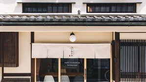 Une entrée typique d’un hôtel japonais traditionnel, avec des portes coulissantes, un auvent en bois à lattes et un dallage en pierre.