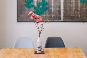 Een tafel met een vaas roze bloemen, een decoratief bord en een schilderij aan de muur.