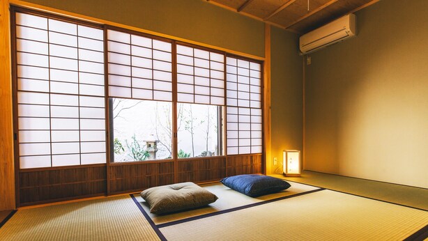 Une pièce de style japonais traditionnel, avec un sol recouvert de tatamis, des paravents shoji et une petite table de chevet surmontée d’une lampe.