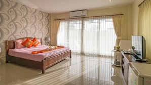 Una habitación de hotel con una cama de madera, televisión, escritorio y un ventanal con cortinas.