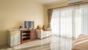 Habitación de hotel moderna con televisión de pantalla plana, mini refrigerador, mueble de madera, sof á blanco y un ventanal con cortinas translúcidas.