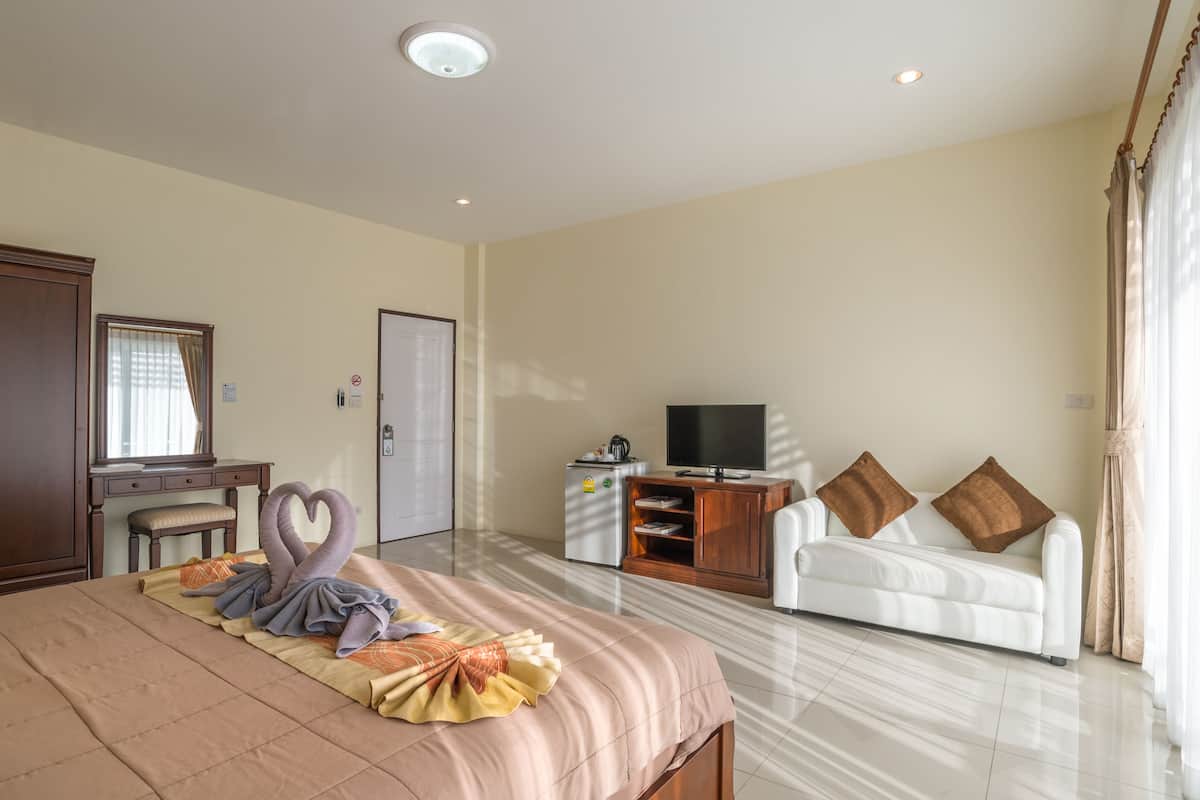A hotel room with a bed, a desk, a television, a sofa, and a minibar.