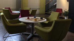 Un espace de détente moderne avec une table ronde et des chaises vertes, un jeu d’échecs et un escalier en arrière-plan.
