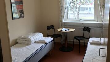 A small, clean room with two single beds, a small table, two chairs, and a window with curtains.