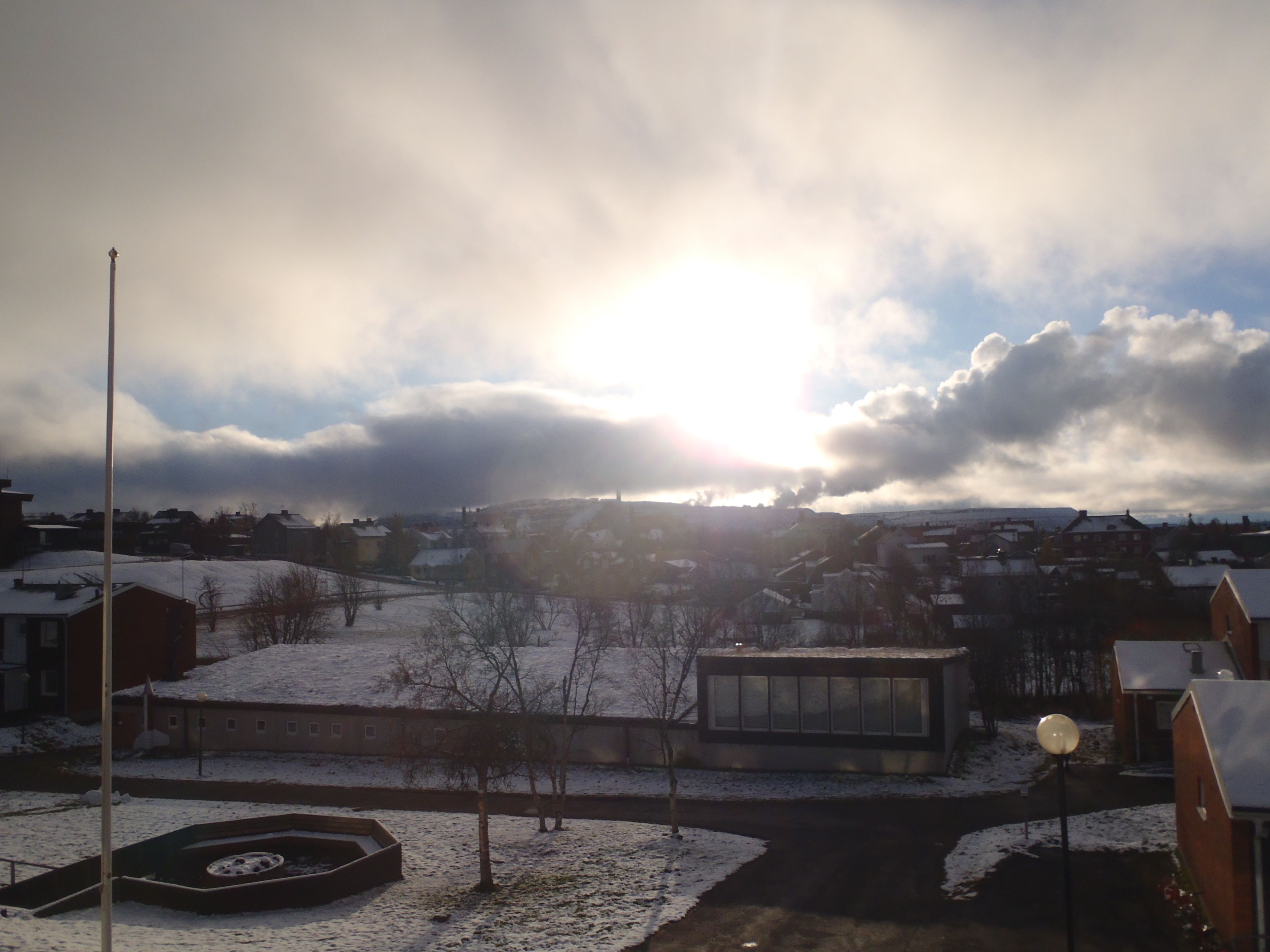 A residential area with houses, a snow-covered landscape, and a clear sky with the sun shining.
