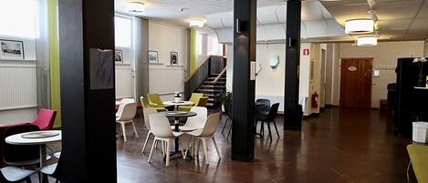 A spacious indoor area with multiple seating arrangements, including round tables and chairs, and a staircase leading to an upper level.