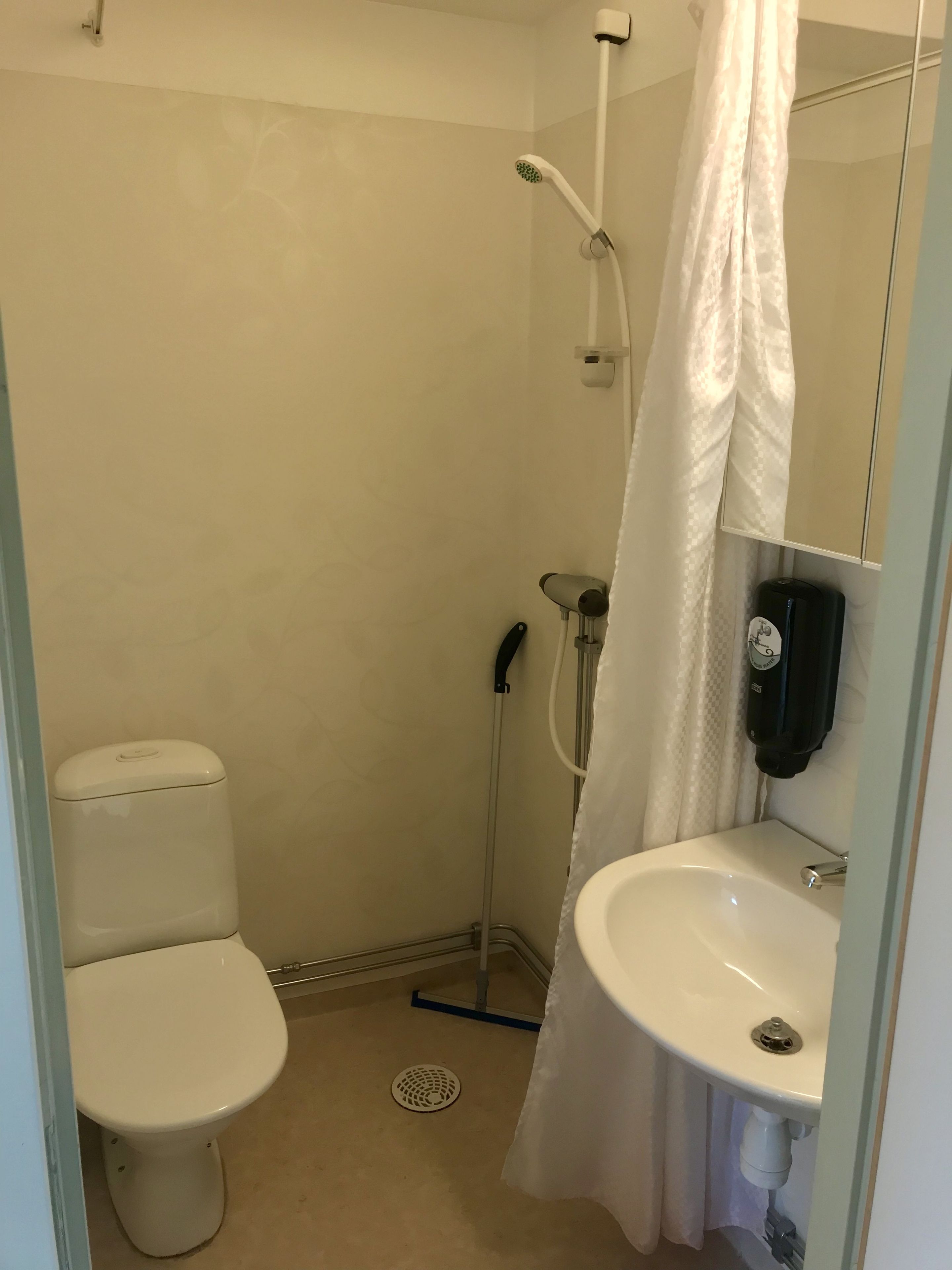 Baño pequeño y funcional con inodoro, ducha con cortina y lavamanos con espejo.