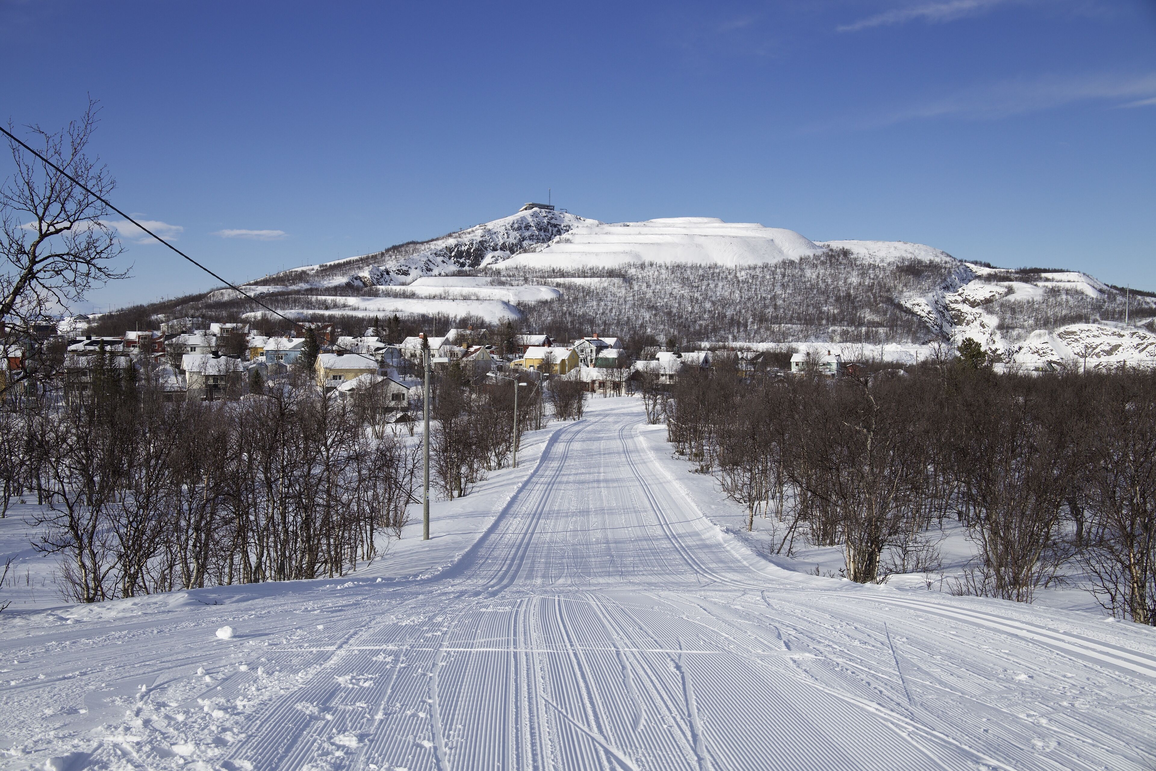 Une route enneigée menant à une montagne, avec des maisons sur le côté gauche.