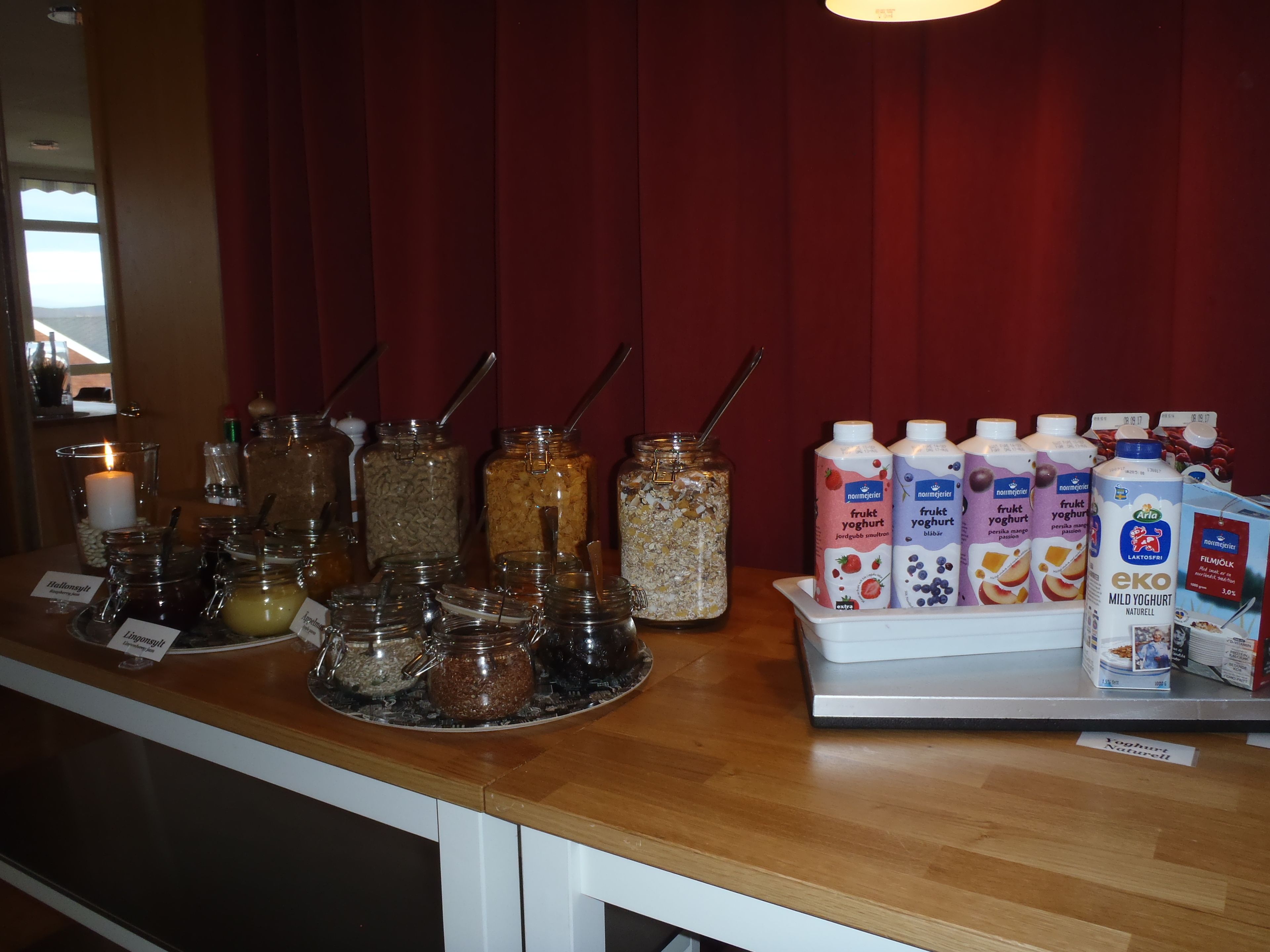 A breakfast bar with various food items and beverages, including jars of granola, honey, and jams, as well as cartons of milk and yogurt.