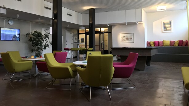 Un hall d’entrée moderne avec des fauteuils jaunes et roses, un comptoir d’accueil et une grande plante.