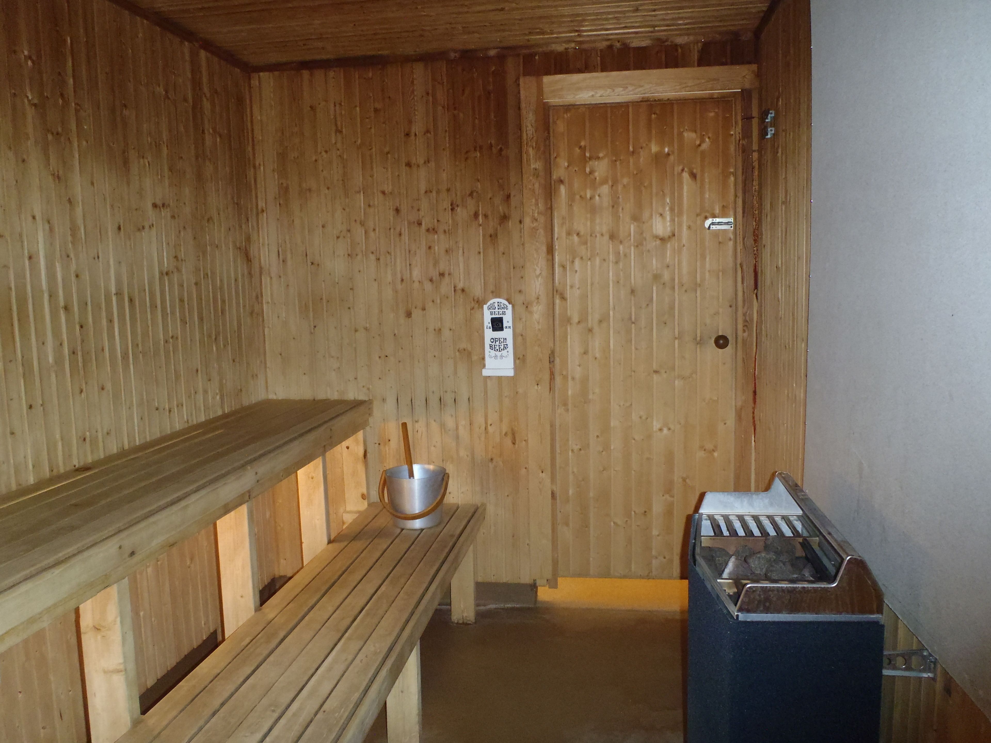 A wooden sauna room with benches, a metal bucket, and a sauna heater.