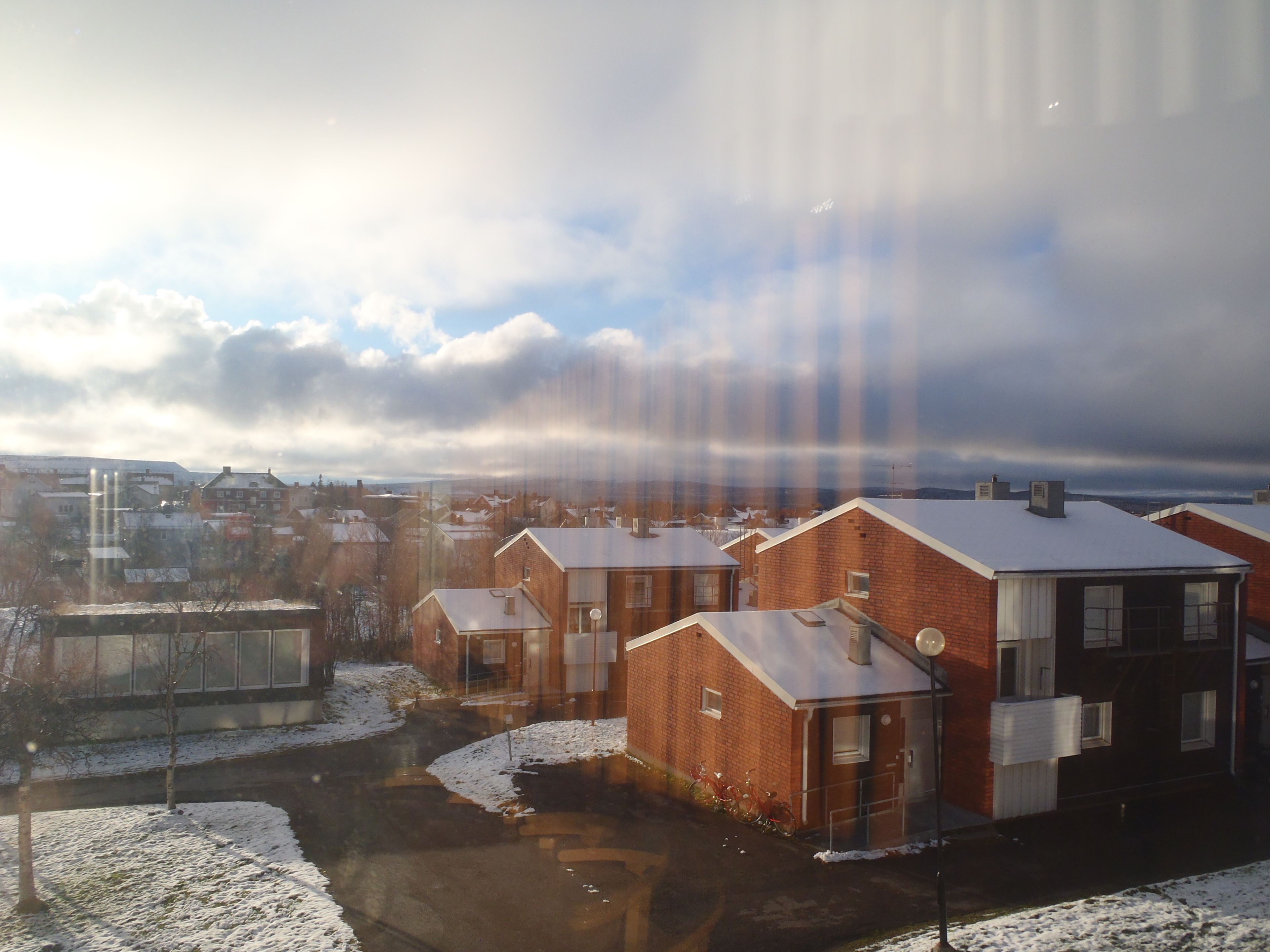 A residential area with brick houses, some with snow on the roofs, and a clear sky with clouds.