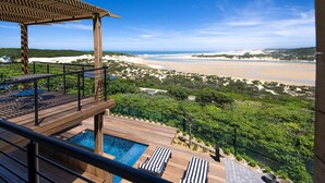 Una terrazza in legno con piscina, sedie a sdraio e vista sulla spiaggia e sulle dune.