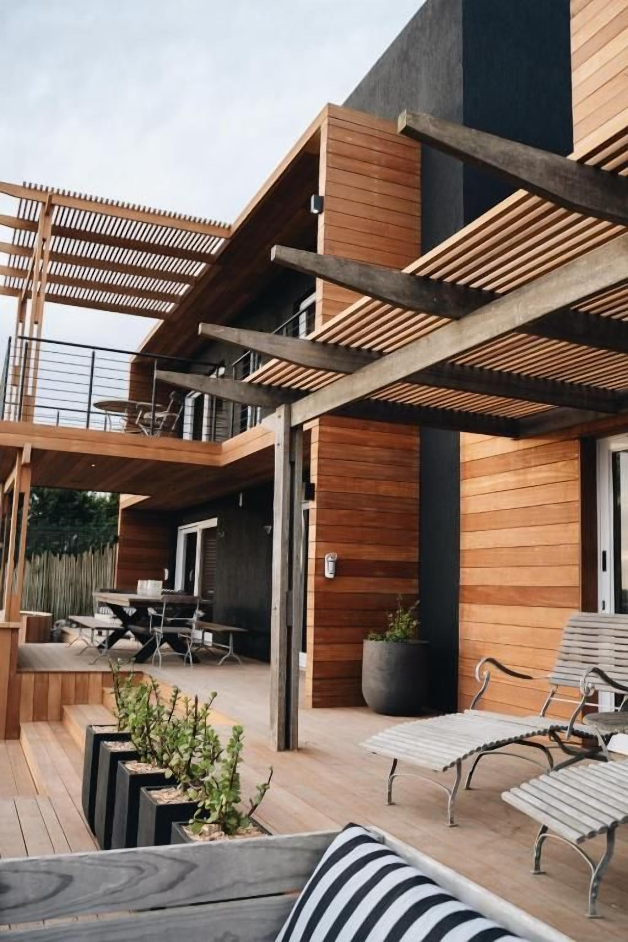 A modern outdoor patio with wooden flooring, metal furniture, and a pergola structure.