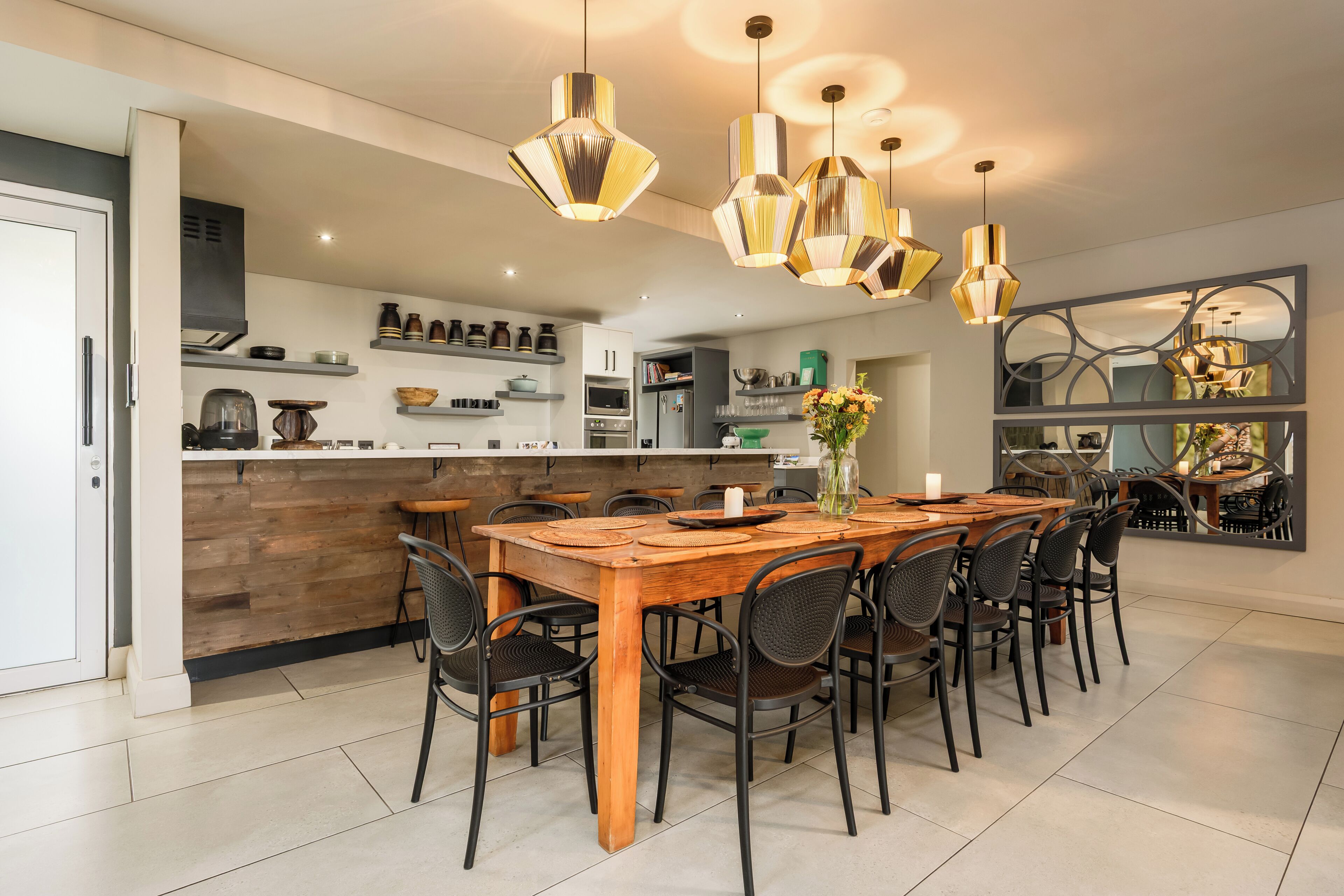 A modern kitchen with a central island, pendant lighting, and a dining area with chairs and a table.