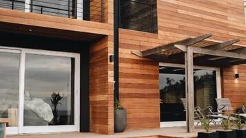 A modern two-story building with a wooden facade, a balcony, and a covered outdoor seating area with striped cushions.
