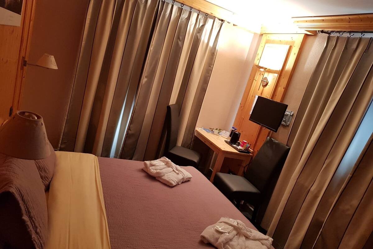 A hotel room with a bed, a desk, a chair, a TV, and curtains.