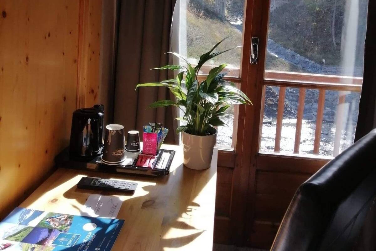 A wooden cabin room with a large window offering a view of a forested valley and a bridge.