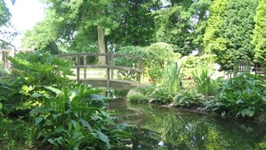 A tranquil garden with a wooden bridge over a pond, surrounded by lush greenery and trees. - TOR Rooms (Canterbury)