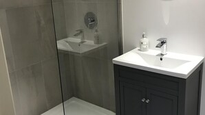 A modern bathroom with a glass-enclosed shower, a white sink, dark cabinetry, and a round mirror on the wall. - TOR Rooms (Canterbury)