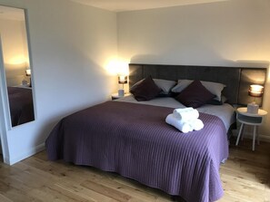 A neatly made bed with a purple bedspread and pillows, a bedside lamp, and a small table with a lamp. - TOR Rooms (Canterbury)