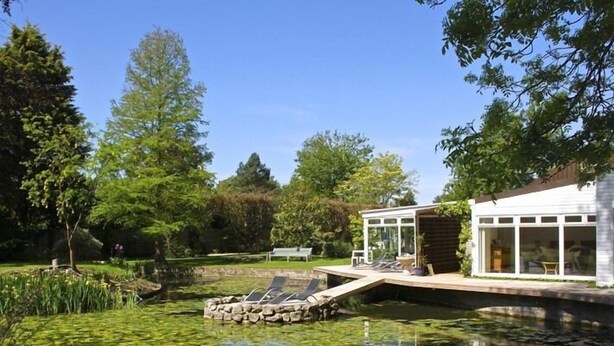 A house with a glass-enclosed porch, a stone bridge over a pond with lily pads, and a well-maintained garden. - TOR Rooms (Canterbury)