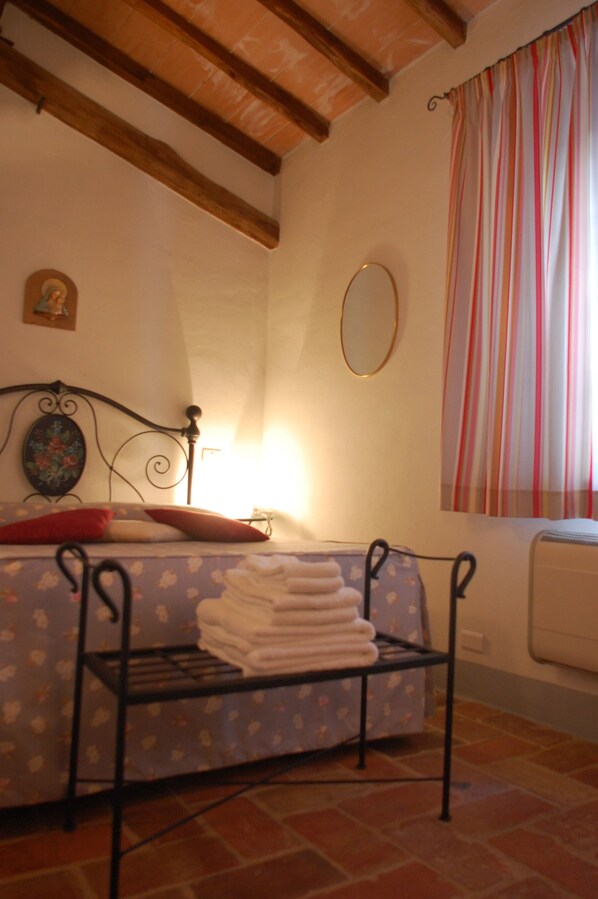 A bedroom with a bed, a bedside table with towels, a mirror, and a window with curtains. - Agriturismo Podere Alberese (Asciano)