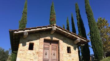A stone building with a wooden door and a small window, surrounded by tall cypress trees.