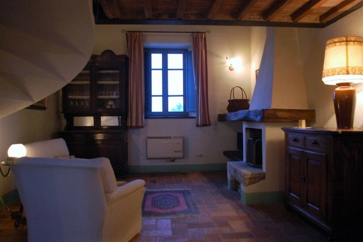 A cozy room with a fireplace, a window with curtains, a lamp, and a cabinet.