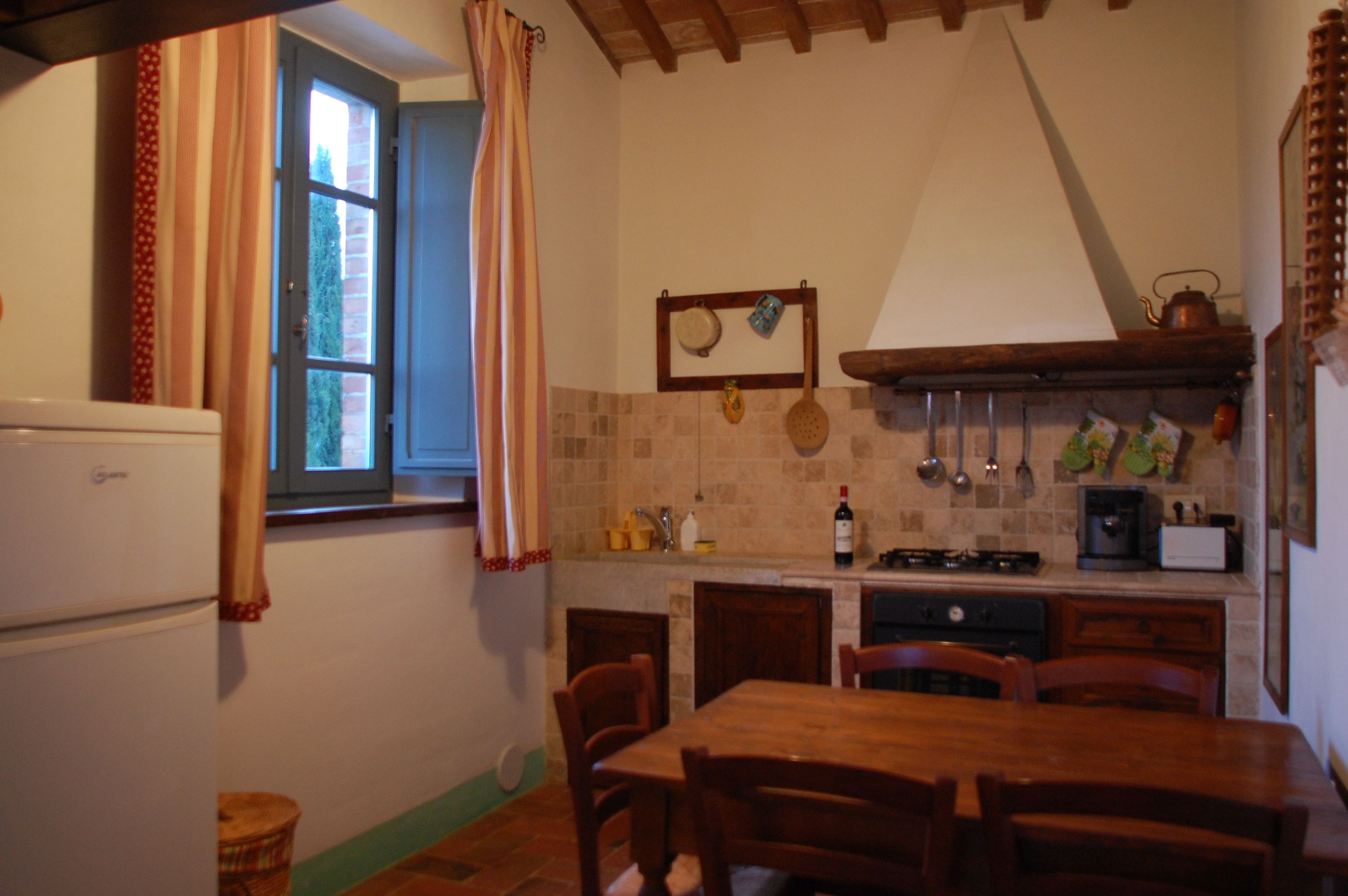 Une cuisine compacte comprenant une table à manger, des chaises, un réfrigérateur, une fenêtre avec des rideaux et un pare-feu en carrelage.