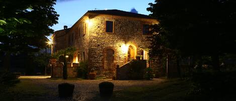 A stone building with a paved entrance and a lit entrance door.