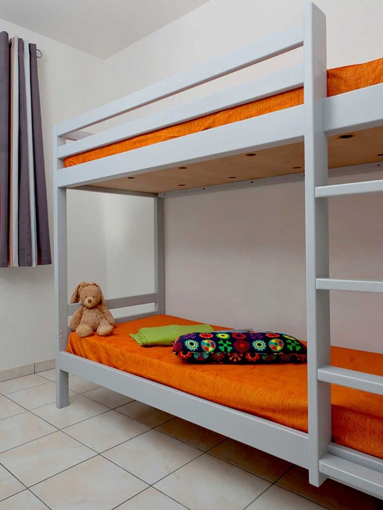 A bunk bed with a teddy bear on the lower bunk and a colorful pillow on the top bunk.