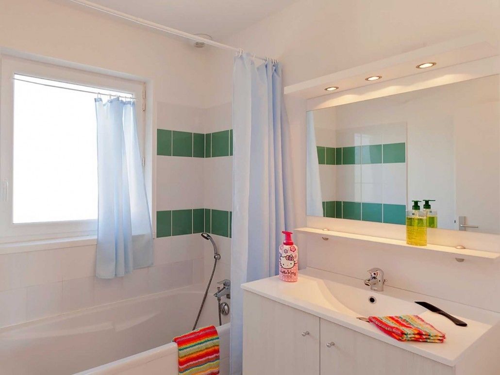A bathroom with a bathtub, a shower, a sink with a mirror, and a window with curtains.