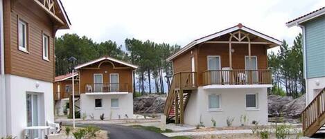 Une rangée de chalets en bois dotés de balcons, une allée de gravier et un paysage boisé en arrière-plan.