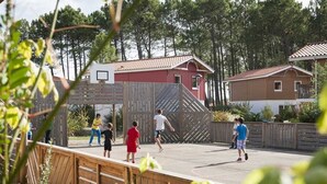 Un groupe de personnes joue au basketball sur un terrain extérieur, entouré de clôtures en bois et de maisons.