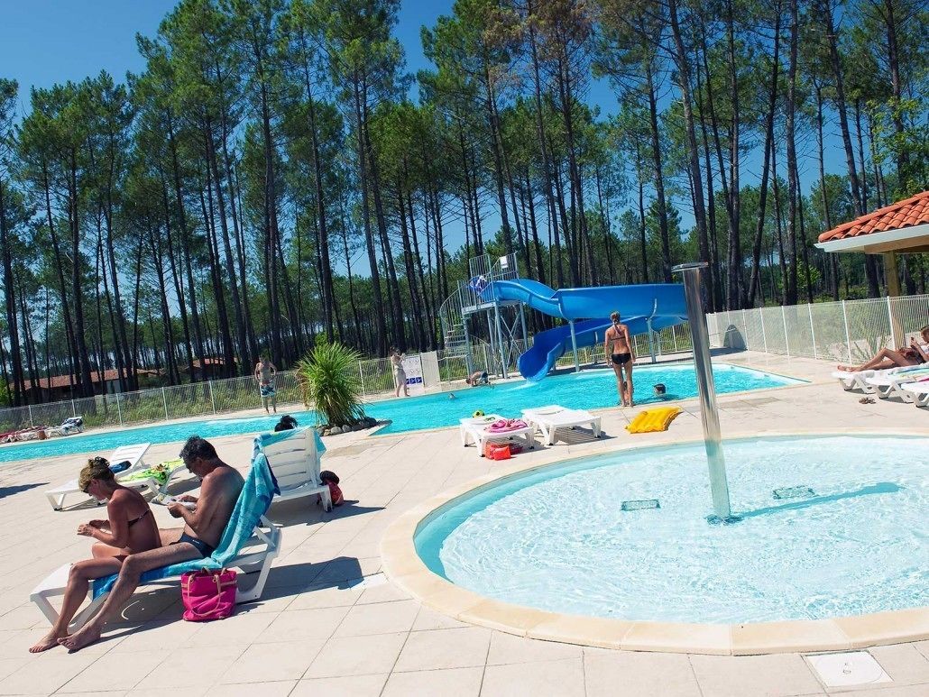 A pool area with lounge chairs, a water slide, and a surrounding forest.