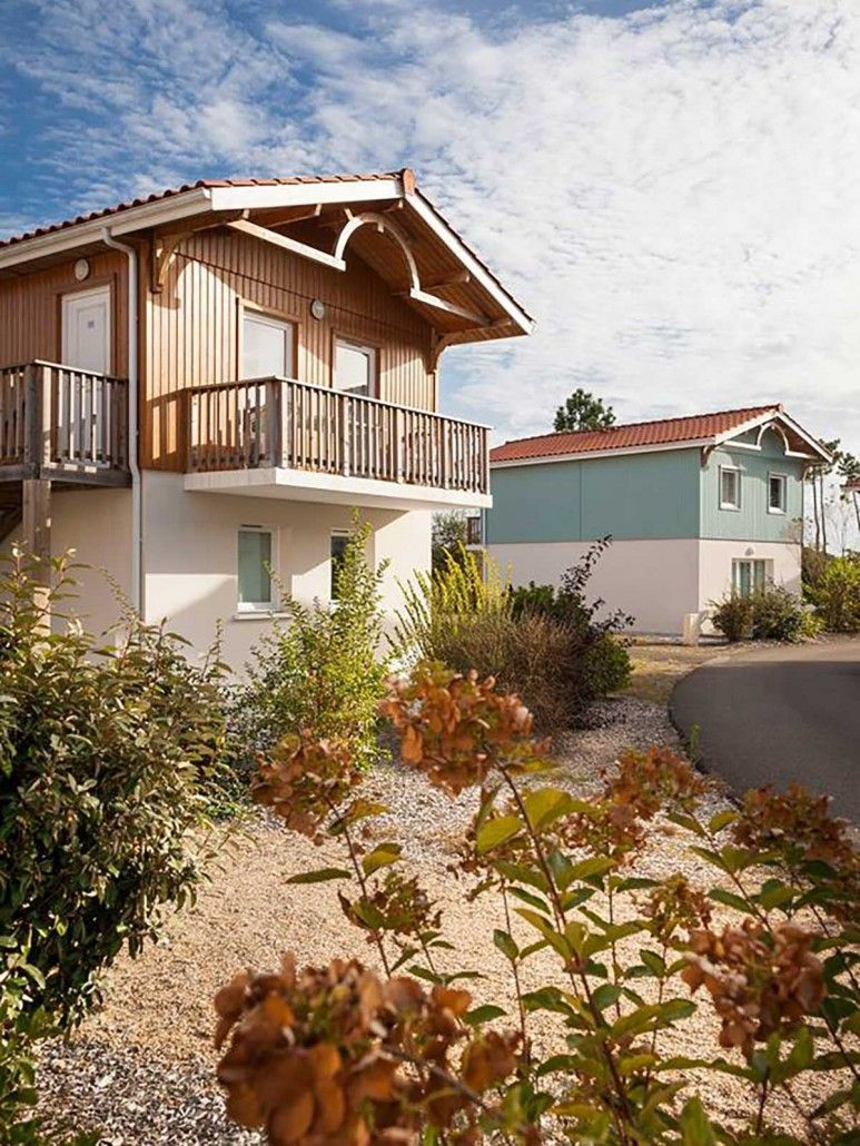 A two-story wooden building with a balcony, surrounded by gravel and plants.