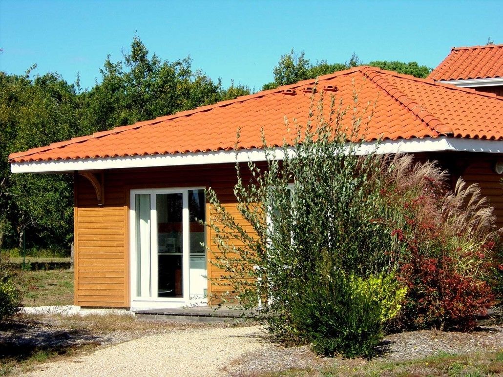 A wooden house with a red-tiled roof, a wooden door, and a gravel driveway.