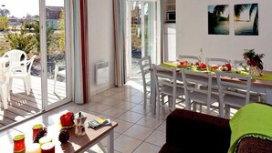 Un salon lumineux avec un coin repas, de grandes fenêtres et une vue sur l’extérieur.