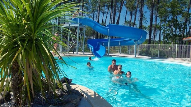 Une piscine avec un toboggan bleu, entourée d’arbres et de rochers.
