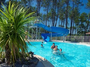 Una piscina con un tobogán de color azul, rodeada de árboles y rocas.