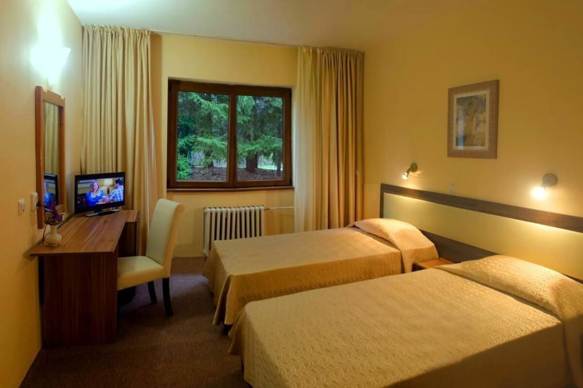 A hotel room with two beds, a desk with a chair, a television, and a window with curtains.