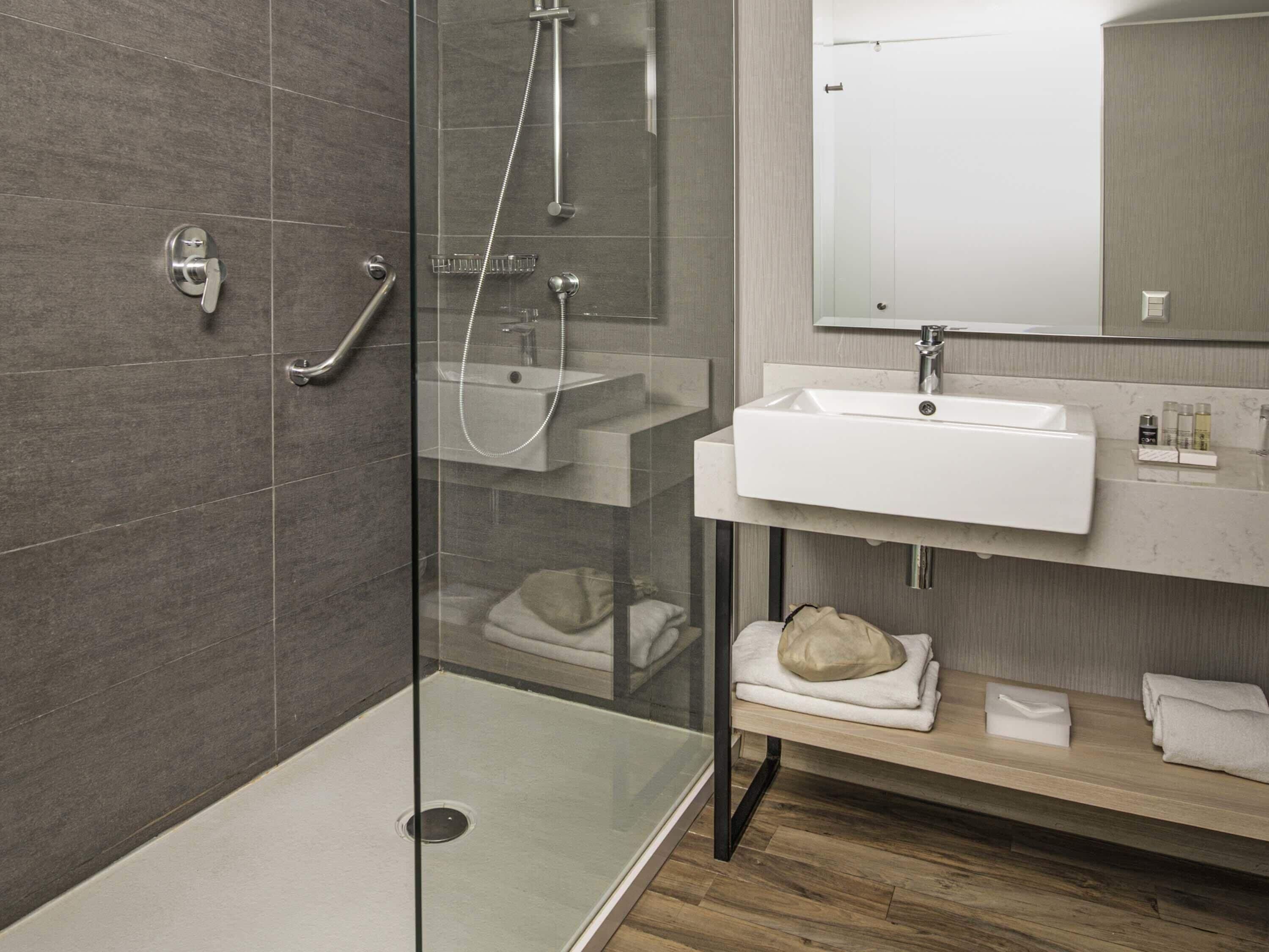 A modern bathroom with a glass-enclosed shower, a sink, and a mirror.