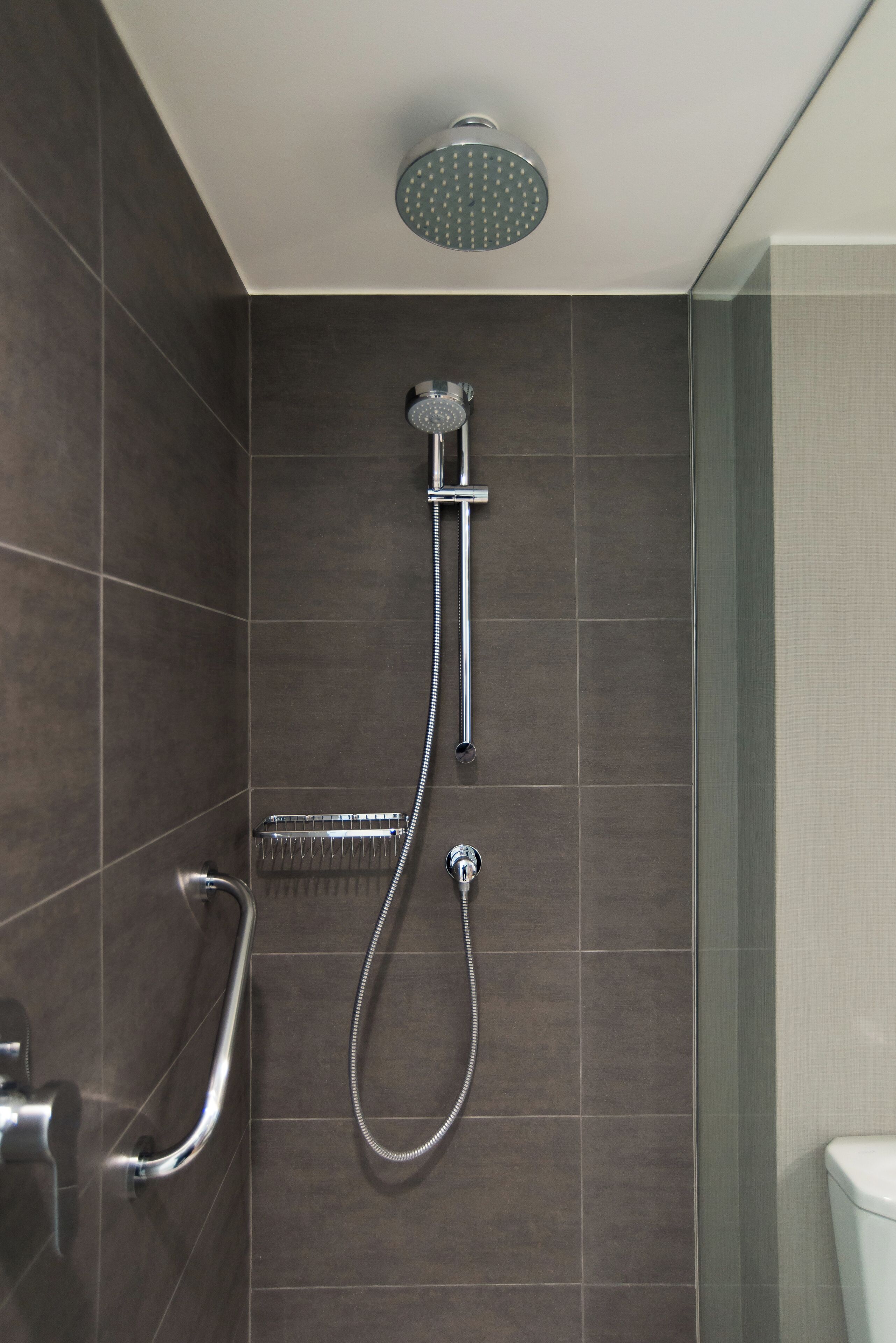 A modern shower area with a handheld showerhead, a fixed showerhead, and a handheld showerhead with a flexible hose.