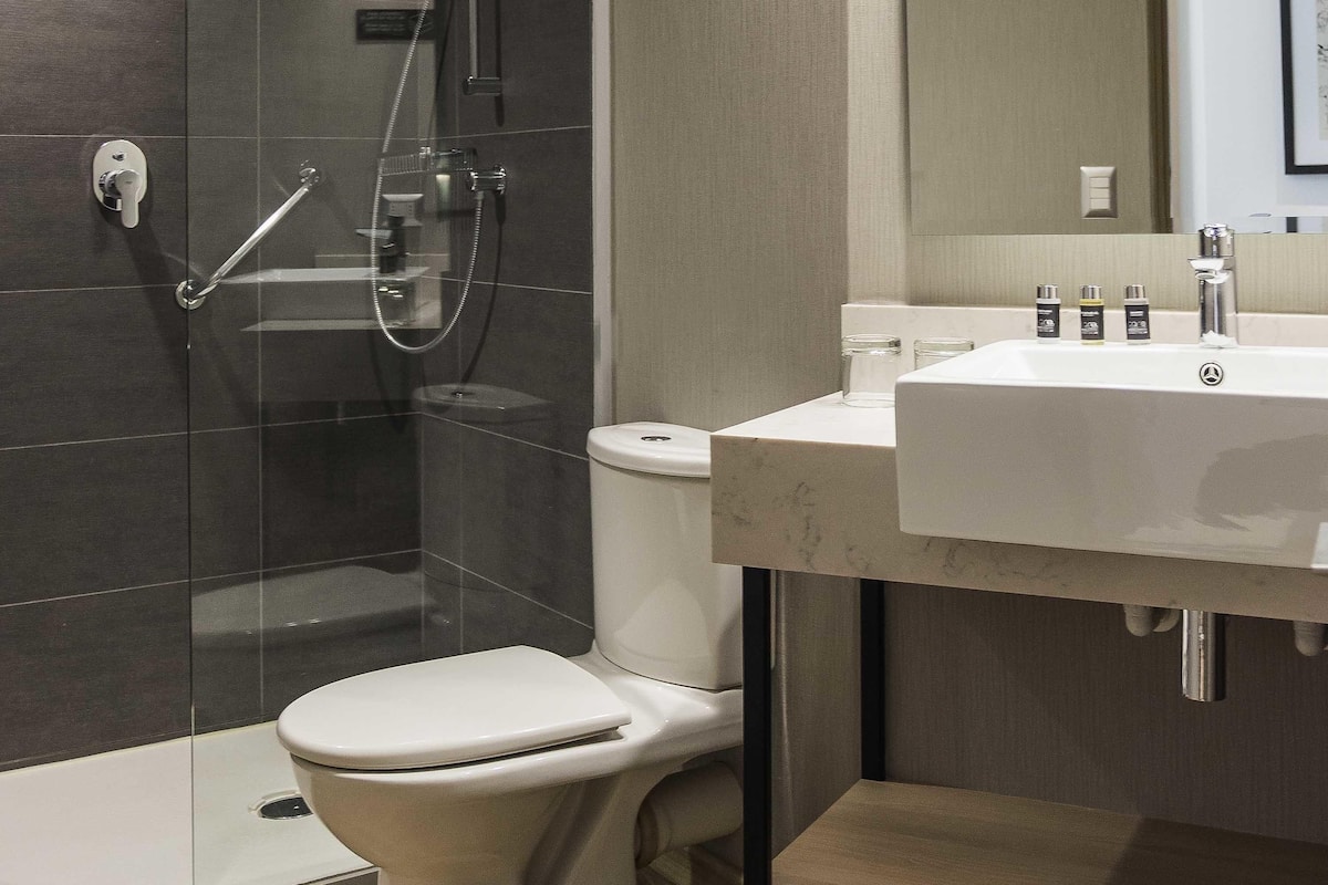A modern bathroom with a glass-enclosed shower, a white toilet, and a sink with toiletries.