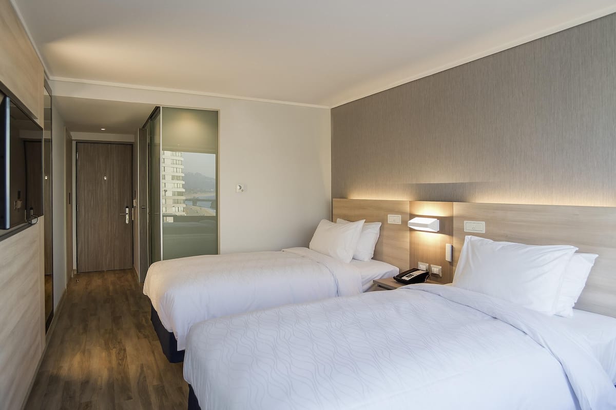 Hotellihuone, jossa on kaksi sänkyä, puulattia, näkymä ovesta ja yöpöytä, jossa on puhelin.