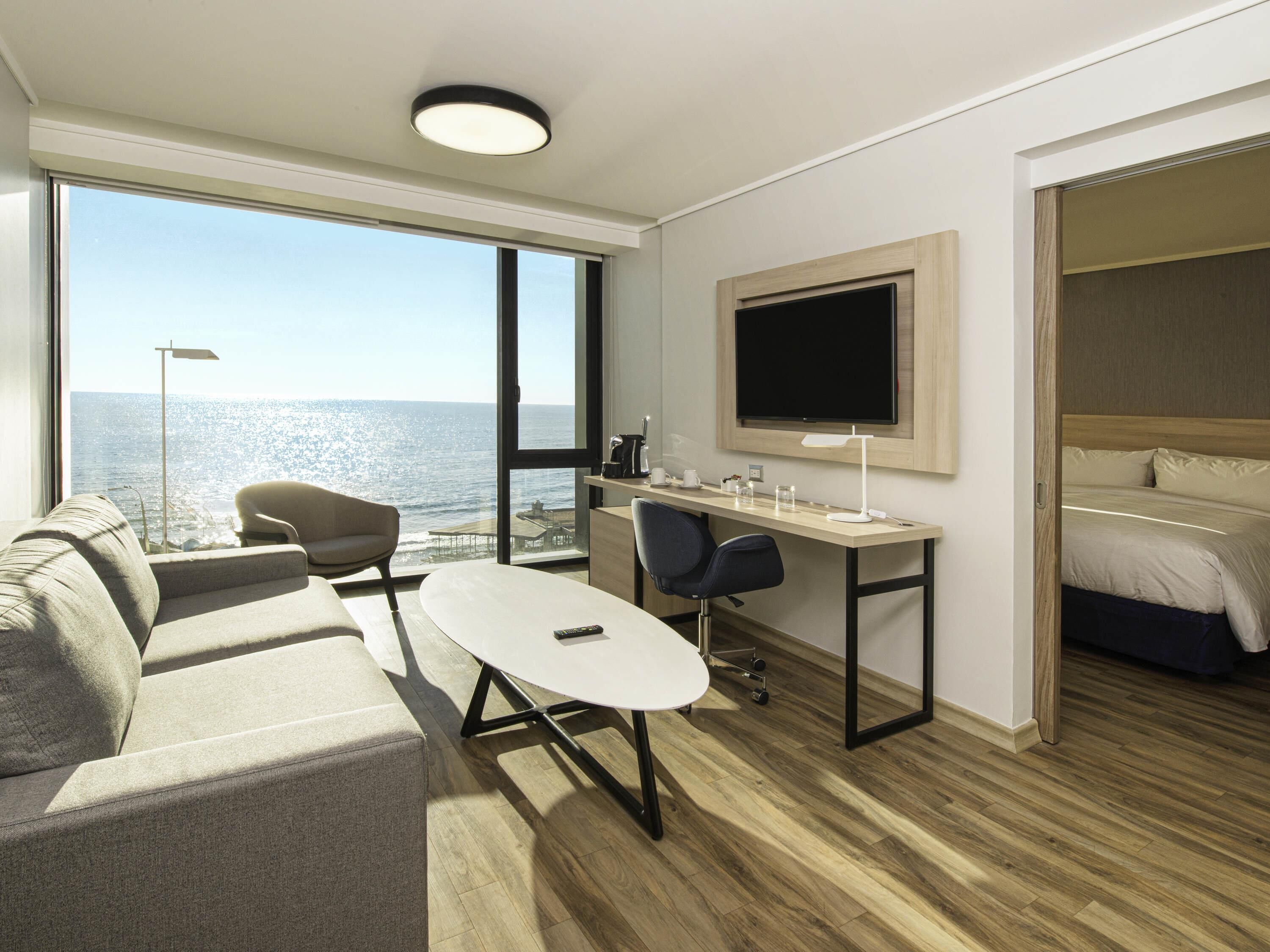 Ein modernes Hotelzimmer mit großem Fenster, Schreibtisch, Sofa, Bett und Fernseher.