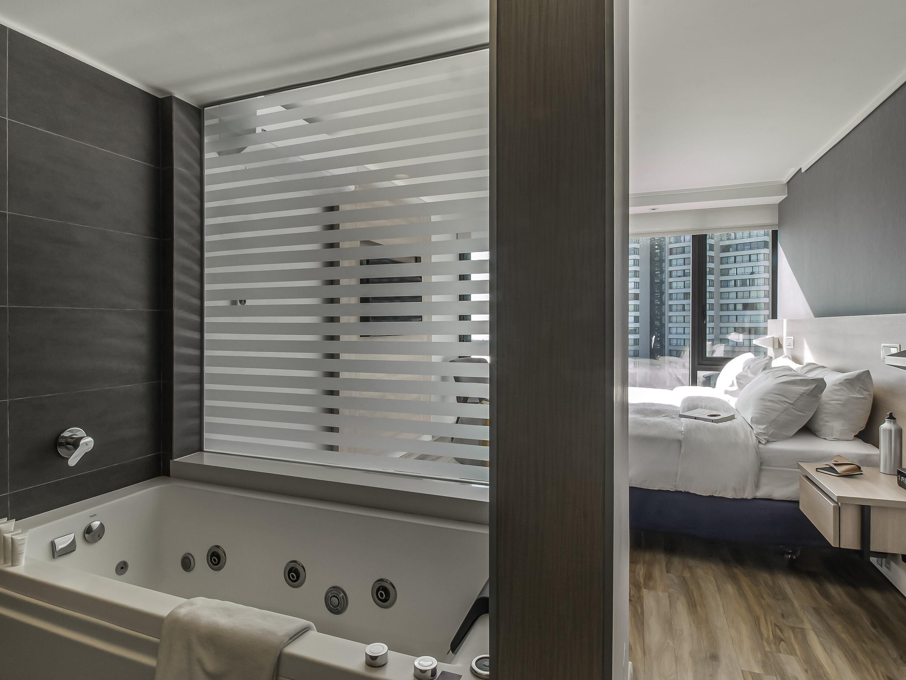 A modern bathroom with a bathtub, a shower, and a window with blinds.